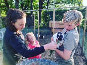 duas crianças e uma mulher a segurar um cabrito bebé em De Skure: vakantiewoning op boerderij em Harelbeke
