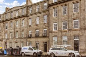 two cars parked in front of a large brick building at 1 Bedrooms Flat in Central Edinburgh Haymarket, Heart of Edinburgh Flat Sleeps 4 , in Edinburgh