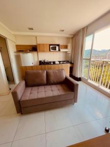 a brown couch in a living room with a kitchen at Flat TOP e PERFEITO inteiro na Barra da Tijuca com cozinha, lavanderia, GARAGEM e wi fi in Rio de Janeiro