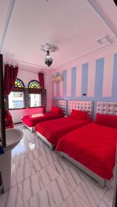 a bedroom with three beds with red sheets and a table at Hotel Sevilla in Chefchaouene