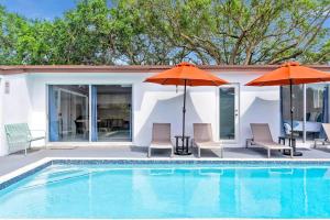 a swimming pool with two orange umbrellas and chairs at Modern Getaway 4BRs House with Pool and Game Room in Hollywood