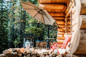 a patio with a table and chairs and an umbrella at Rocky Mountain Escape Log Cabin Rentals - Rock Lake in Rock Lake Lodge Provincial Park