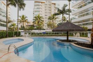 a large swimming pool with a umbrella and palm trees at Paraíso na Riviera São Lourenço - Laguna Home Resort in Riviera de São Lourenço