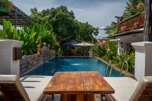 a pool with a wooden table in front of a house at Antonios Villa Hotel in Siem Reap