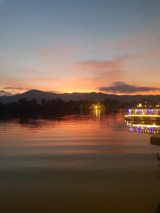 a sunset on a lake with lights on the water at The Hideaway in Kampot