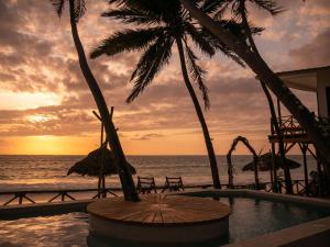a sunset at the beach with a pool and palm trees at KIMA Serviced Beach House & Suites in Bwejuu