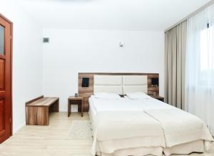 a white bedroom with a large bed and a desk at Hotel Sphinx in Żabia Wola