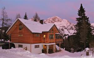 ein Holzhaus im Schnee mit einem Berg in der Unterkunft Almhaus Nassfeld in Sonnenalpe Nassfeld