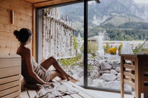 a woman sitting on a window sill looking out at the mountains at Hotel Riederalm in Leogang