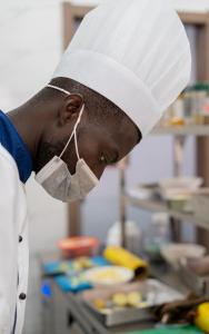 un homme portant un chapeau de chef et un masque dans l'établissement G.C ROYAL HOTEL, à Accra