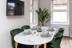 a white dining room with a white table and green chairs at Ocean Studio Apartments in Littlehampton