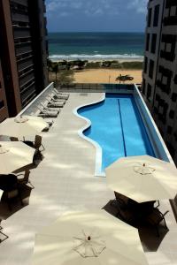 a swimming pool with umbrellas and chairs and the beach at Flat Beach Class Executive in Recife