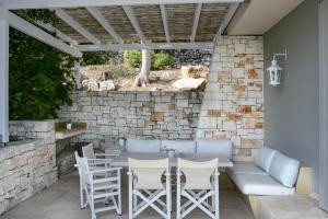 a patio with a table and chairs and a stone wall at Apeiron II Villa by PaxosRetreats in Oziás