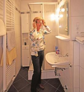 Eine Frau, die im Bad steht und in den Spiegel schaut. in der Unterkunft Appartement Haus Salzburg in Bad Füssing