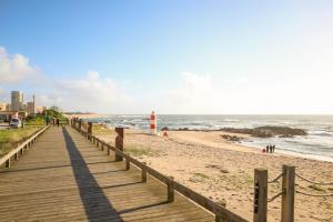 eine hölzerne Promenade, die zu einem Strand mit einem Leuchtturm führt in der Unterkunft Casa Fragosa - Alojamento local in Póvoa de Varzim