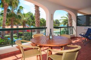 una mesa de madera y sillas en un balcón con palmeras en UHC Costa Linda Family Complex, en Hospitalet de l'Infant