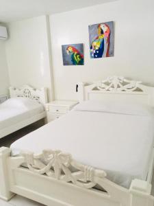 a white bedroom with two beds and paintings on the wall at PLAYA LAGUITO in Cartagena de Indias