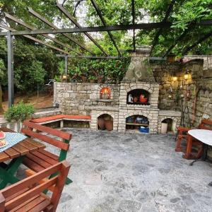 um pátio com uma lareira de pedra com uma mesa e bancos em Apartmani Paulino em Herceg Novi