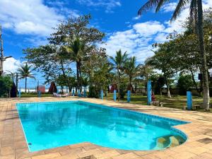 a blue swimming pool with palm trees in the background at Chalé Jorai - pé na areia in Bertioga