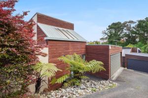 a house with a wooden wall and a palm tree at Elegant 2BR Family Home - Aircon - 5min to Beach in Auckland