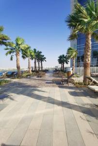 a sidewalk with palm trees and benches and a building at Gharfar 31715 Serene Teal theme-high floor-Pool in Dubai