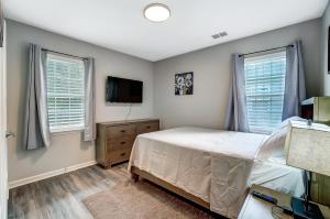 a bedroom with a bed and a tv and two windows at Cozy, 1-Level Cottage - 5 miles to Uptown CLT in Charlotte