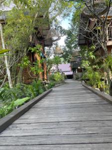 a wooden walkway in a garden with trees and plants at The Temak Villa in Pantai Cenang