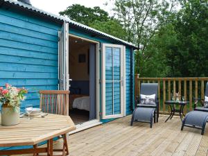 a blue shed with a table and chairs on a deck at The Shepherds Hut in Herstmonceux