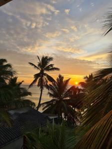 a sunset with palm trees in front of the ocean at Frangipani Beach Villa in Tangalle