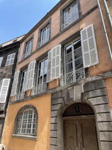 un edificio con ventanas blancas con persianas y una puerta en Luxueux 2 pièces 65m2 Hôtel Particulier XVII ième siècle-Centre Historique Clermont-Ferrand en Clermont-Ferrand