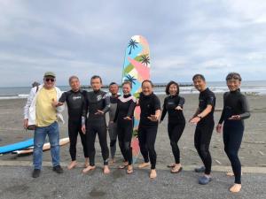 um grupo de pessoas de pé na praia com uma prancha de surf em オーシャニア一宮 em Ichinomiya