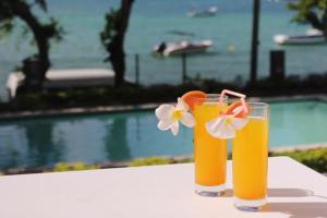 two glasses of orange juice sitting on a table next to a pool at Valmarin Seafront Apartments in Trou dʼ Eau Douce