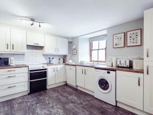 a kitchen with white cabinets and a washer and dryer at Stable End Cottage in Bouth