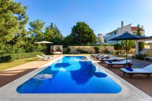 a pool with chairs and umbrellas next to a house at Kallithea Breeze Luxury Villa in Koskinou