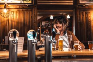 Uma mulher sentada num bar com copos de cerveja. em Hotel Cornelyshaff em Heinerscheid