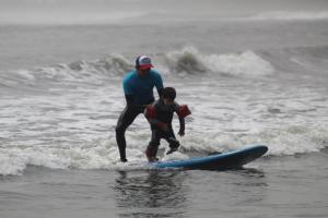 un hombre y un niño en una tabla de surf en el océano en Totora Surf Hostel, en Huanchaco