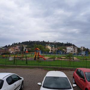 three cars parked in a parking lot in front of a playground at Jednosoban stan Zoja in Podgorica