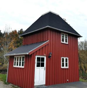 eine rote Scheune mit einem schwarzen Dach und einer weißen Tür in der Unterkunft Birkevang The Silo - Rural refuge in Faxe