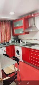 La cuisine est équipée de placards rouges, d'une table et d'un évier. dans l'établissement Apartamento en el centro de OVIEDO, à Oviedo