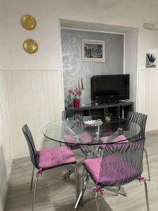 een glazen tafel met stoelen met roze kussens en een televisie bij CAPOLINEA in Roccalumera