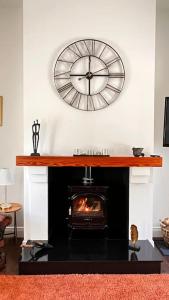 a clock on the wall above a fireplace with a stove at Rectory Cottage. Close to Enniskillen and lakes. in Enniskillen