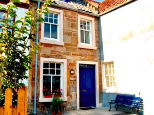 una casa de ladrillo con una puerta azul y un banco en Neuk Hoose, en Crail