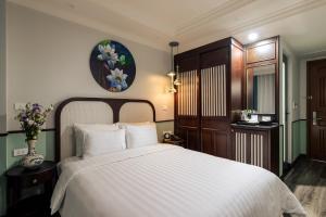 um quarto com uma cama branca e um vaso de flores em Lotusama Hanoi Hotel em Hanói
