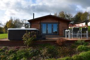 a small cabin with a deck with chairs and a table at Long Wood Lodges in Knighton
