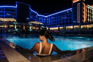 una mujer sentada en una piscina por la noche en Maxeria Blue Didyma, en Didim