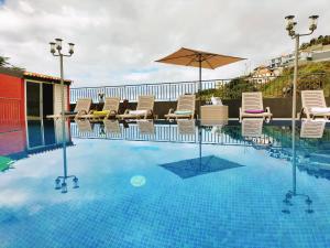 a swimming pool with chairs and an umbrella at Villa Fanny in Ribeira Brava