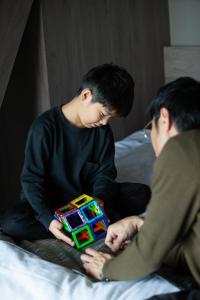 Dois homens sentados numa cama a brincar com um brinquedo. em FAV HOTEL KAGOSHIMACHUO em Kagoshima