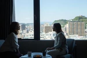 twee vrouwen in een kamer die uit een raam kijken bij FAV HOTEL KAGOSHIMACHUO in Kagoshima