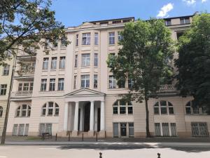 un grand bâtiment blanc avec un arbre en face dans l'établissement Apartament Aleja 22, à Poznań