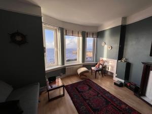 a living room with large windows and a person sitting in a chair at Anchorage, a lovely 2nd floor one bedroom apartment with fabulous seaviews in Largs